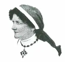 Profile of a woman wearing a nurse's uniform and headscarf, with a larged beaded cross necklace