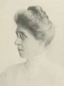 A middle-aged white woman with her hair in a bouffant updo, wearing eyeglasses and a high-collared white lace-trimmed blouse or dress
