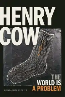 A photograph of a woven sock with "HENRY COW" in large type in the top left, "THE WORLD IS A PROBLEM" in smaller type in the bottom right, and "BENJAMIN PIEKUT" in small text in the bottom left