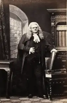 Standing portrait of Henry Bagshawe wearing judge's wig and formal dress, left hand on a vertical book