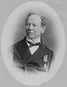 Head and shoulders image of a fair-skinned middle-aged man, wearing mid-Victorian business suit, with a medal on the left chest