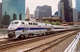 A gray diesel locomotive with a blue stripes and two thinner red stripes on the side. The stripes narrow and angle downwards on the front.