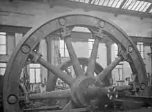 Flywheel; the hub and spokes cast in two halves, bolted at the hub with the rim assembled from ten castings. These are bolted to the spokes, held together by shrinking rings in the grooves.