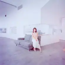 A picture of Hikaru Utada sitting in a greyish living room.