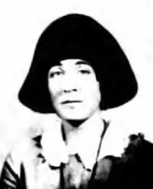 A black-and-white passport photograph, depicting a white woman wearing a large black hat, and a dress with a round white collar