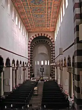 The interior of another long narrow church with high windows. The arch leading into the chancel at the far end has alternating red and white stones.