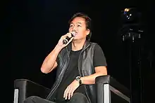 A man sitting in a chair and speaking in a microphone.