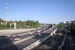 Photograph of a section of rail tracks next to a freeway exit ramp with busy a six-lane freeway to the left