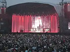 A man, performing on a stage in front of a capacity crowd.