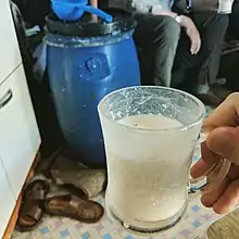 A glass of airag in front of the plastic barrel used to make it