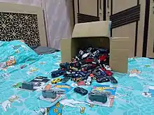 A cardboard box full of Hot Wheels cars spilling into a blue bed.
