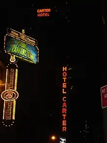Nighttime view of the Hotel Carter. There are four illuminated signs in the picture: two signs reading "Hotel Carter" to the right, and two signs for the Hilton Theatre (now the Lyric Theatre) to the left.