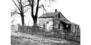 a log cabin on the side of a hill in black-and-white. White writing runs along the bottom.