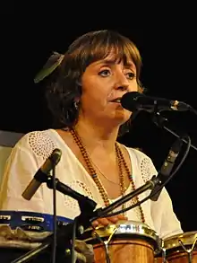 white female seated behind set of hand drums, with a microphone in front of her