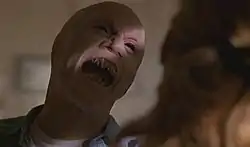 A mutant human with black eyes, sharp fangs, and no ears prepares to attack a woman.