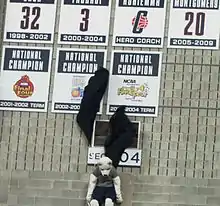 Connecticut Huskies mascot Jonathan pulling down two black curtains, unveiling placards honoring the 2002–03 and 2003–04 women's basketball national championship teams