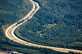 Aerial view of a divided highway making two turns in a densely forested area.