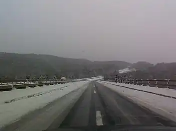 A snowy highway road that is icy and looking toward forests and mountains.