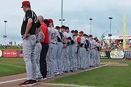 Men in mostly gray baseball uniforms lined up on baseball field's foul line