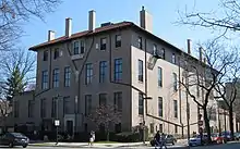 A large pink two story building with a gently sloped peaked roof, seen from across an intersection at a three-quarter angle on a sunny day