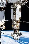 A photograph of two modules, one large and one small, attached to a space station with the Earth visible underneath