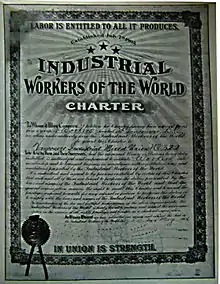 Framed, formal document featuring various IWW themes, cursive body text, hand-filled forms and a stamped seal.