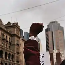 A raised fist can be seen amidst a Black Lives Matter protest, with various Melbourne landmarks in the background