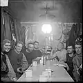 Adolf Lindstrøm, Sverre Hassel, Oscar Wisting, Helmer Hanssen, Roald Amundsen, Jørgen Stubberud, and Kristian Prestrud in the hut at Framheim. Roald Amundsen is resting his elbow on a camera.