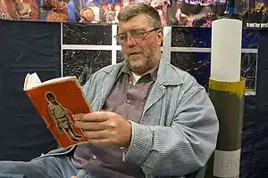 Man with beard wearing striped jacket and glasses sitting reading