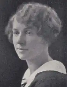 A young white woman with wavy blondish hair cut in a bob, wearing a dark top with a white collar