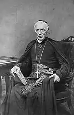 A smiling seated man in Roman Catholic priest's vestments.