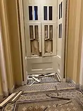 A photo taken from the inside of the Capitol building. Windows are broken, along with their wooden frames. They are boarded up.