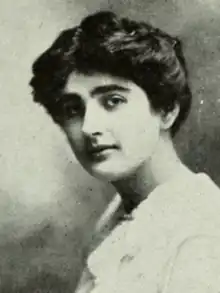 A young white woman with dark hair and eyes, wearing a white lace-collared dress or blouse