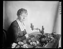 An older white woman, seated at a table with a microscope and ore specimens