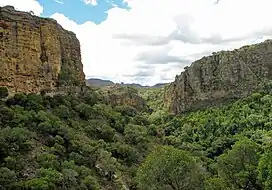 Two huts, wooded grasslands, and an escarpment with deep canyons