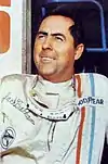 Jack Brabham wearing a racing suit and smiling upwards