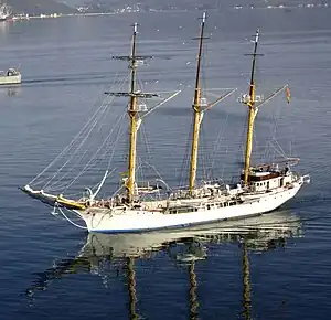 A colour photograph of a white-hulled sailing ship in a bay