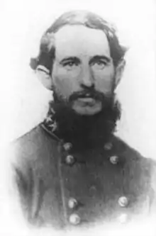 Photo shows a bearded man wearing a dark gray military uniform with two rows of buttons.