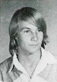 A portrait photo of a white teenager with shoulder-length hair; he has a neutral expression and is facing right of the camera.