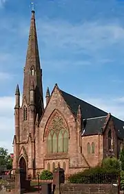 a red sandstone church with a tall spire and a large pointed arch window