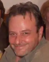 A portrait shot of a smiling, dark-haired man with dark brown eyes.