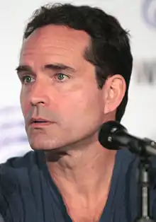 A close-up portrait of Jason Patric behind a microphone.