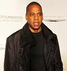 An Afro-American man wearing a black leather jacket and black t-shirt stands before a white background.