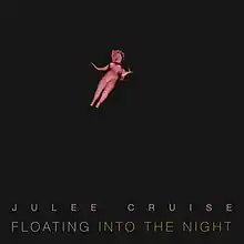 A porcelain doll floating against a black background. Pink block text with wide kerning below reads "Julee Cruise"; grey block text placed below reads "Floating", followed by gold block text reading "into the Night".