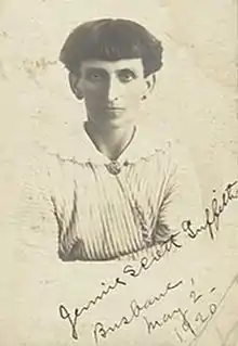 Photograph of a woman with bobbed hair wearing a striped dress with a wide, white, scalloped collar adorned with a broach at the base of her neck.