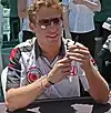 Jenson Button wearing a white T-shirt and holding a pen in both of his hands