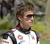 Jenson Button wearing black sunglasses and white and black racing overalls with sponsors logos