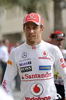 Jenson Button wearing a red baseball cap and white racing overalls with sponsors logos