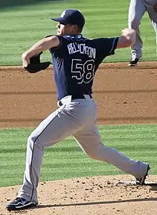A man in a navy blue baseball jersey and cap and gray pants
