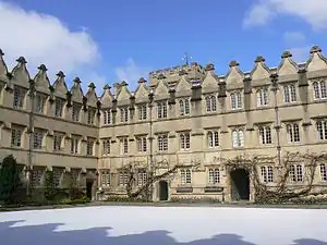 A regular pattern of windows and gables on two sides of a quadrangle of buildings; the matching shadows of the gables on the wall behind the photographer are visible on the snow